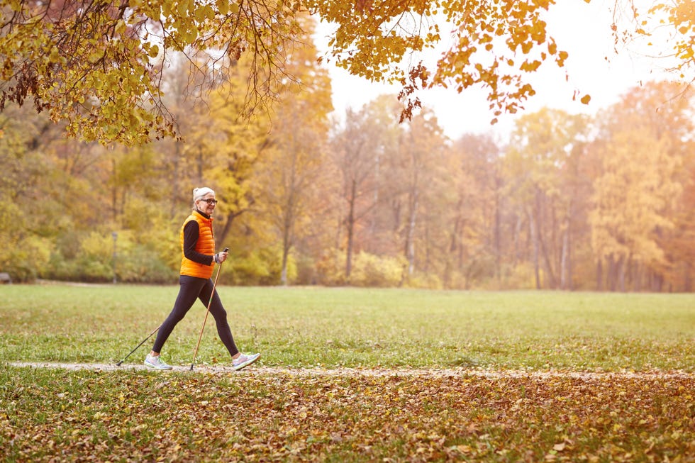 senior female nordic walker walking on autumn park path