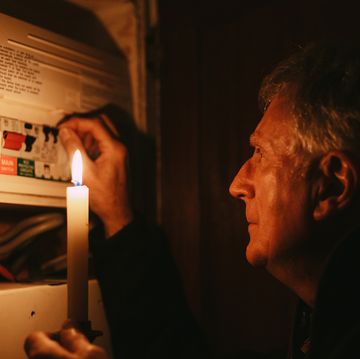 senior man checking home fuse box by candlelight during power outage
