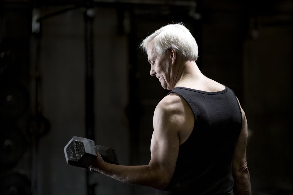 senior man doing bicep curls with dumbbell in dark gym