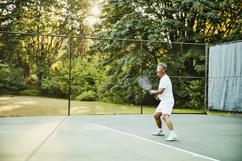 senior man playing tennis during early morning match