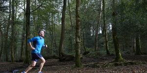 Senior man running through woodland.