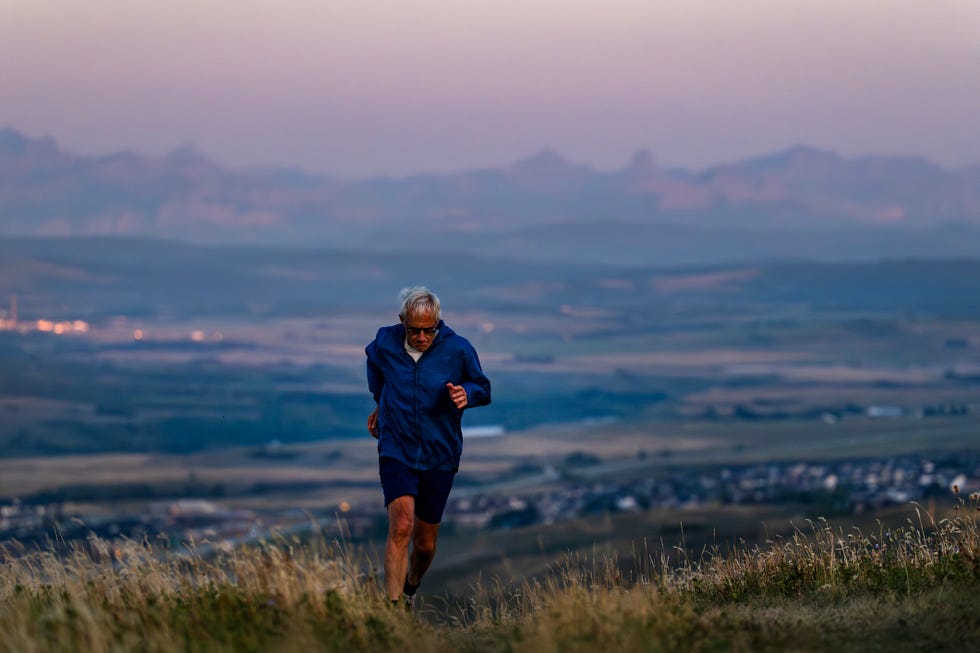 senior man runs through grasses at sunset