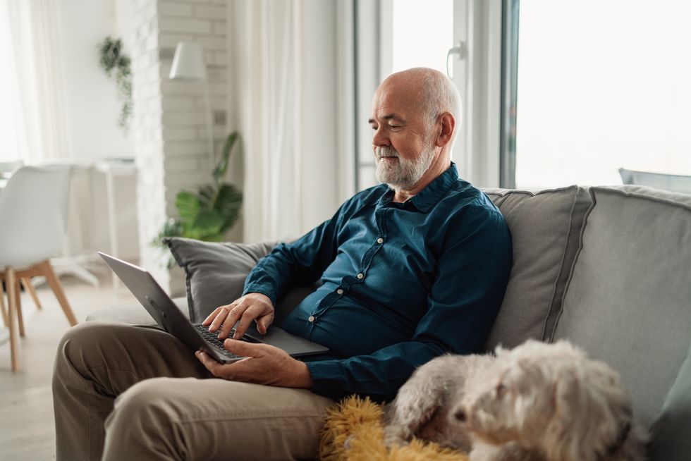 senior man sitting on sofa with his dog and using laptop at home
