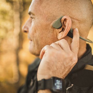 senior man wearing bone conduction headphones to listen music on forest walk or hike close up