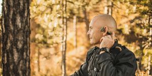 senior man wearing bone conduction headphones to listen music on forest walk or hike