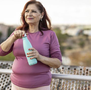 senior plus size hispanic woman drinking a bottle of water in a public park