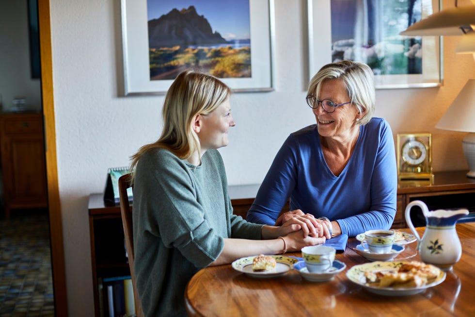 senior woman and young woman sitting at dining table holding hands