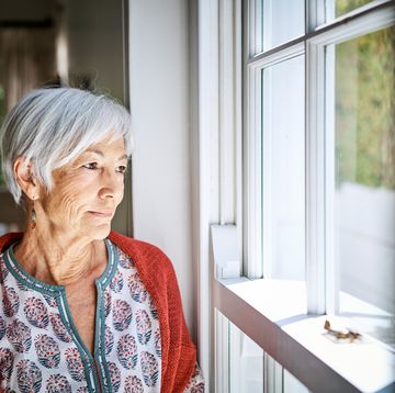 senior woman standing alone by a window at home