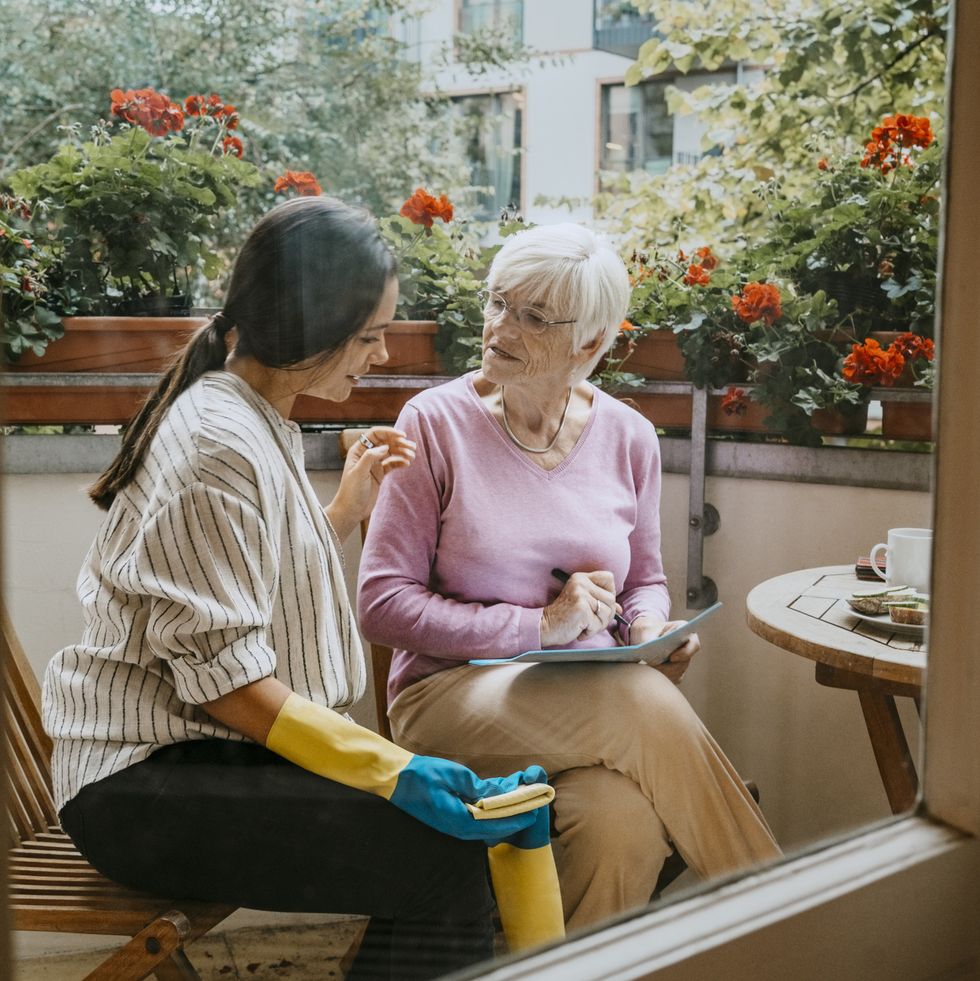 senior woman talking with female caregiver seen through window of balcony