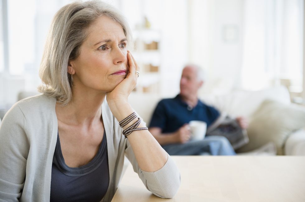 senior woman unhappy, husband in background