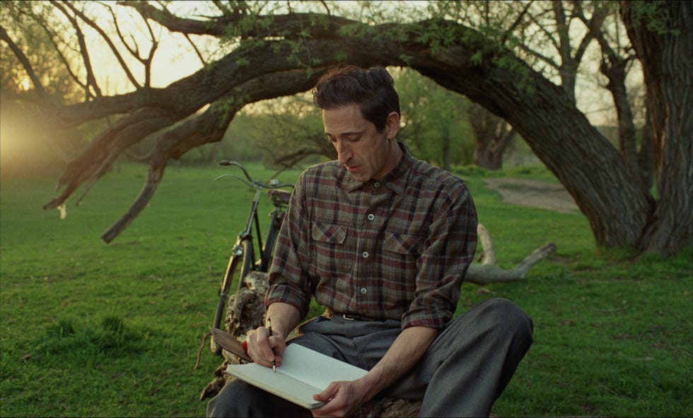 a person writing in a notebook while seated outdoors near a bicycle