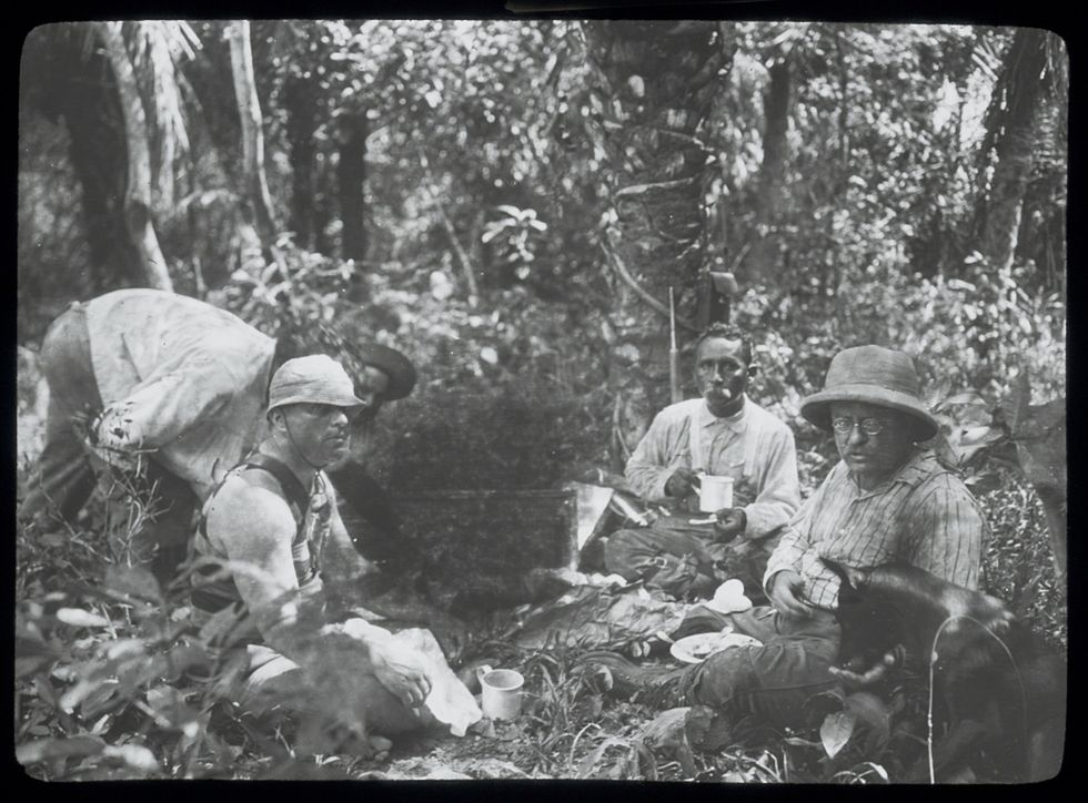 Theodore Roosevelt sitting in camp dog eating from his hand and Brazilian officer Candido Rondon seated at his left during the RooseveltRondon Scientific Expedition to Brazi