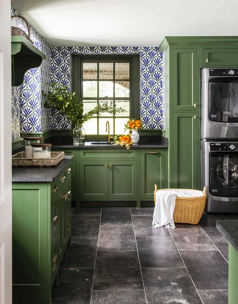 a laundry room with green cabinets and blue and wallpaper with a sink and washer and dryer and laundry basket