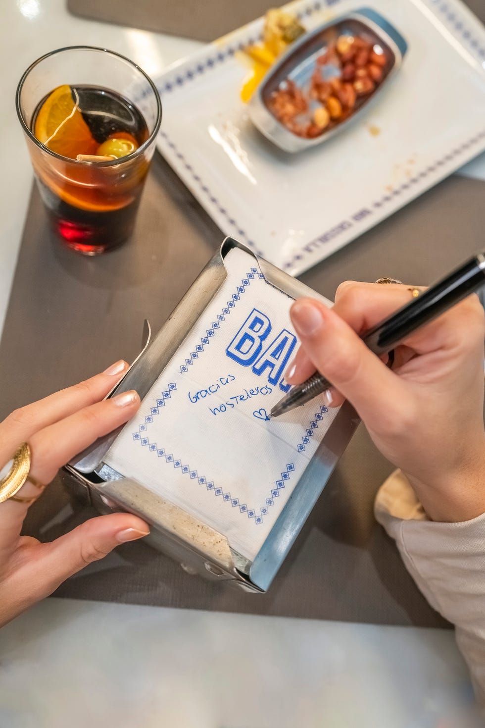 una persona escribe gracias hosteleros en una servilleta de bar