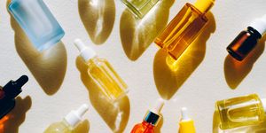 set of many different glass bottles with cosmetic liquids on white surface play of light creates abstract patterns from shadows and illuminating yellow reflections trendy colors of the year 2021 flat lay style
