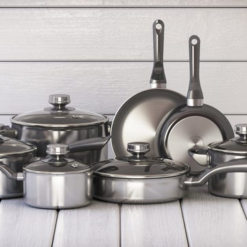 set of stainless pots and pan with glass lids on the white wooden background