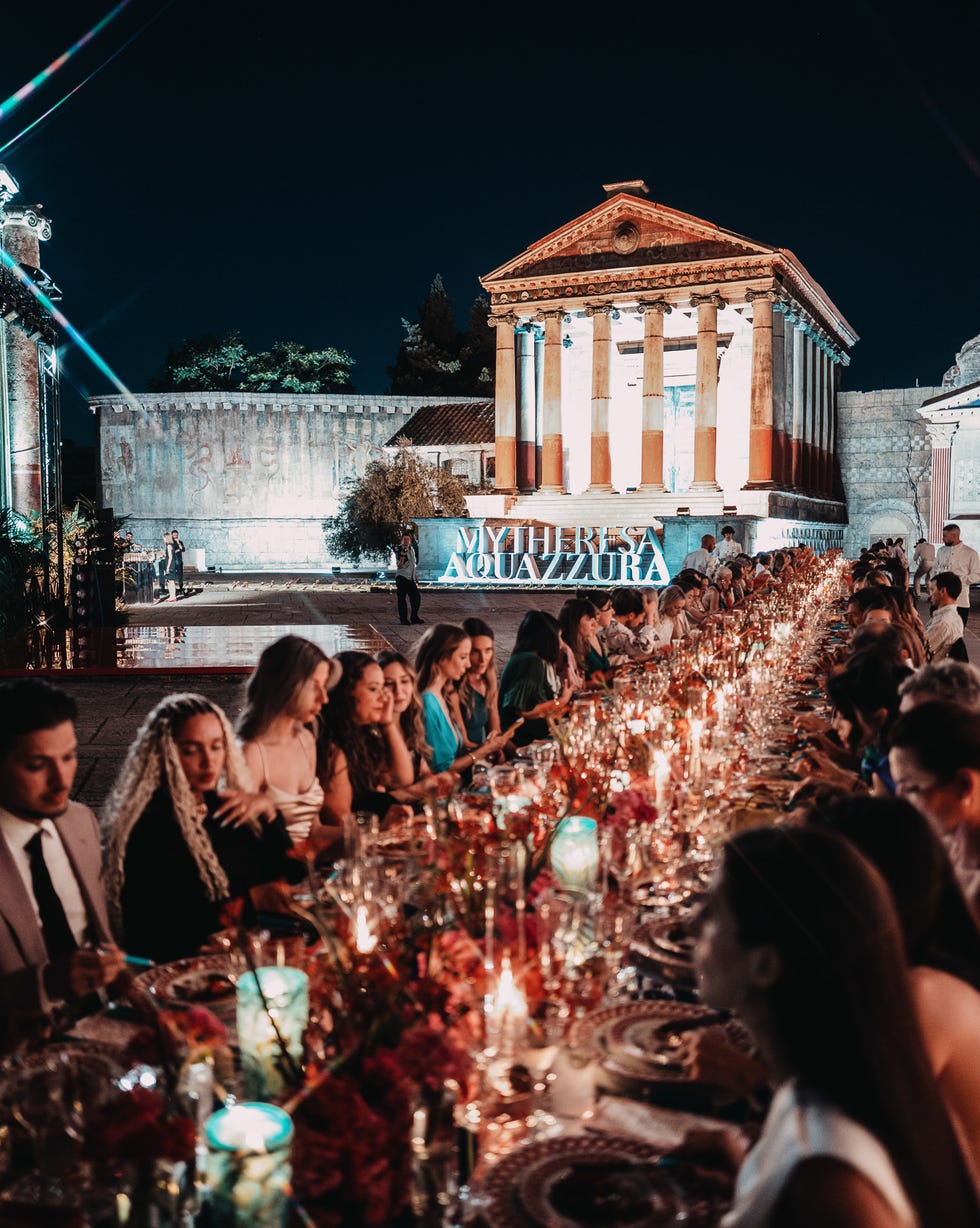 An elegant outdoor dining event at night featuring a long table with decorated settings and a prominent building backdrop