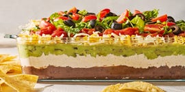layered dip with refried beans, sour cream, guacamole, cheese, tomatoes black olives, and lettuce in a clear dish