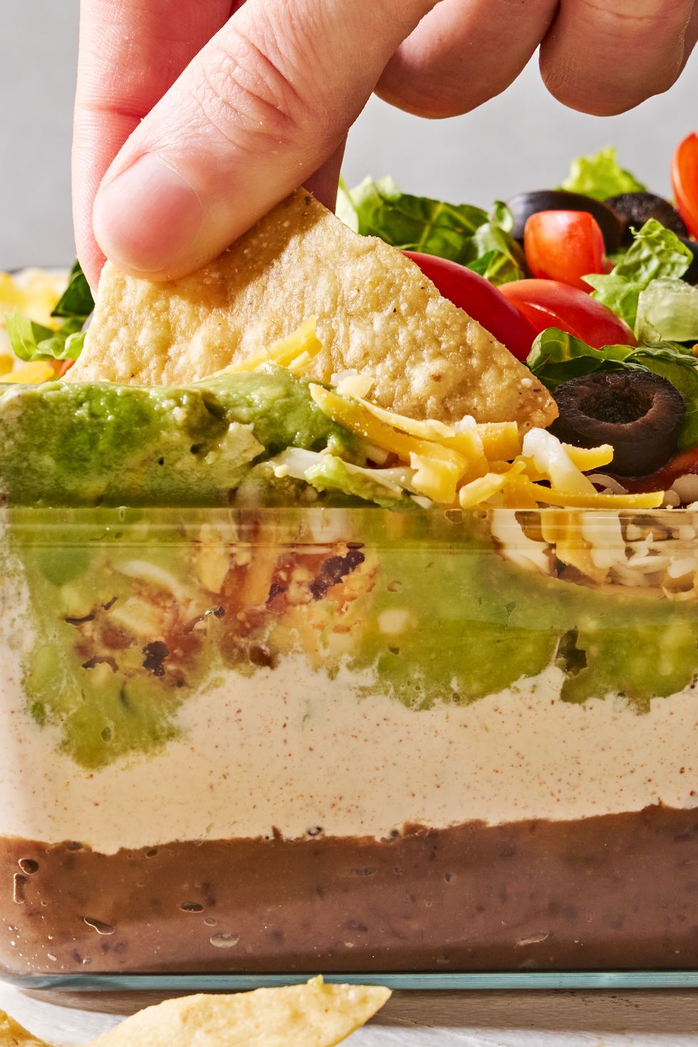 layered dip with refried beans, sour cream, guacamole, cheese, tomatoes black olives, and lettuce in a clear dish