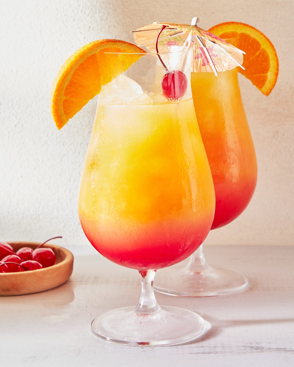 ombre sex on the beach cocktail in a glass garnished with a maraschino cherry, a paper umbrella, and an orange slice