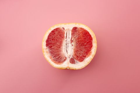 sexuality, erotic tension and metaphor for female sexual organs concept with grapefruit isolated on pink background