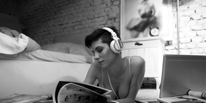 black and white photo of a woman lying on the floor wearing headphones and flipping through magazines