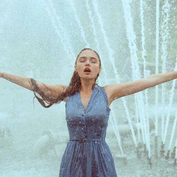 Sexy wet woman with arms outstreched in water drops of fountain