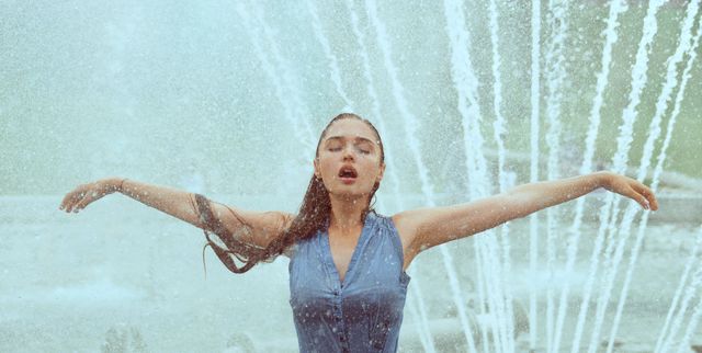 Sexy wet woman with arms outstreched in water drops of fountain