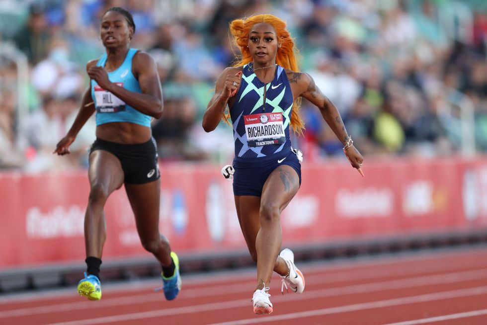 sha'carri richardson run on a track in a skintight blue uniform, another woman running is in the background