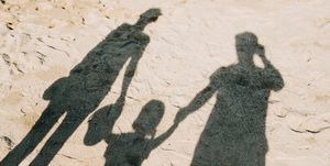 shadow on sandy beach of a loving family of three holding hands relaxing on a lovely sunny day