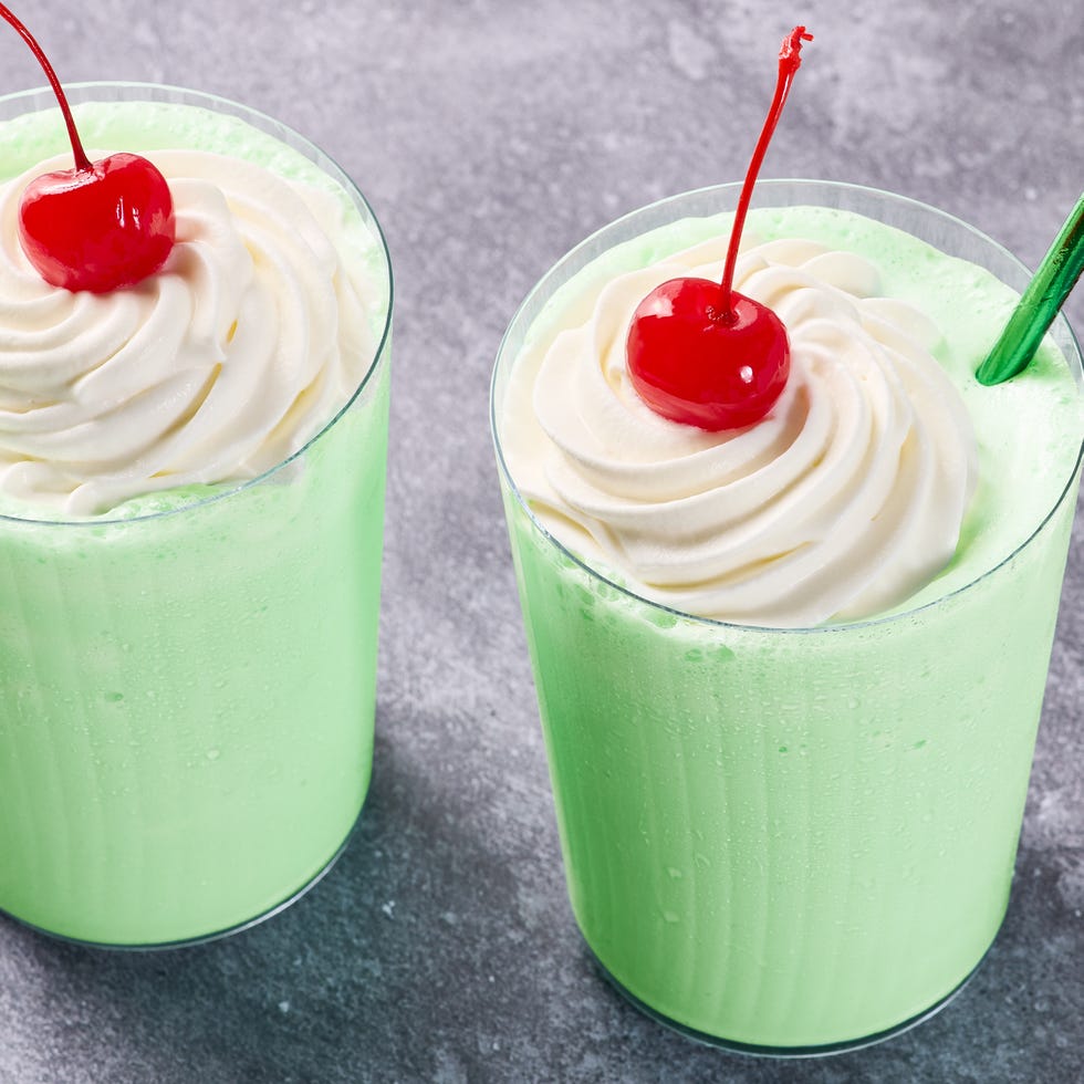 green shake in a glass with whipped cream, a cherry, and a green straw