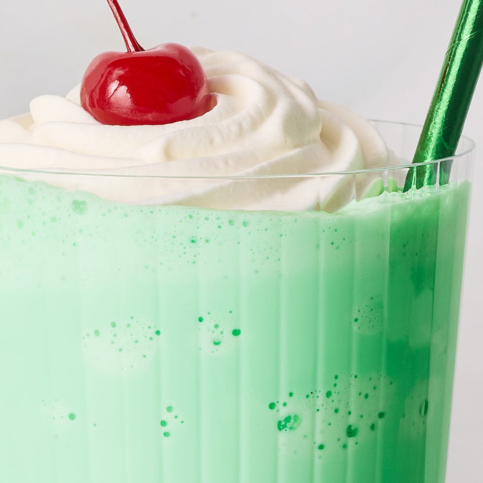 green shake in a glass with whipped cream, a cherry, and a green straw