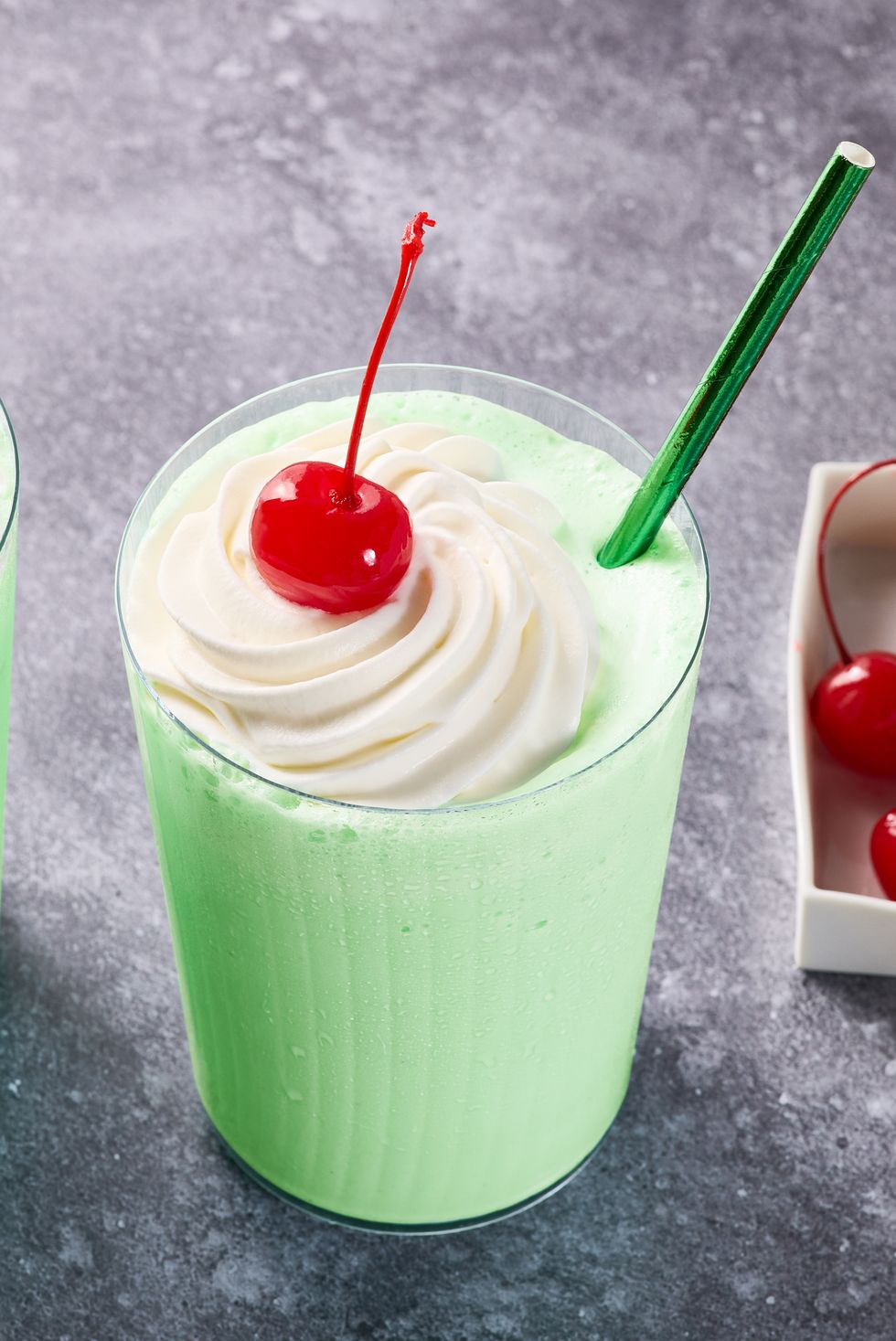 green shake in a glass with whipped cream, a cherry, and a green straw