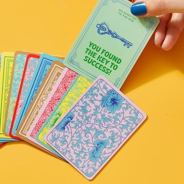 woman pulling 'key to success' card from a pile of game playing cards on yellow background