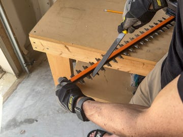 a person wearing gloves sharpening a hedge trimmer blade