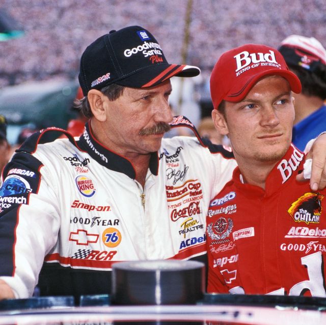 dale earnhardt embracing dale earnhardt jr as they stand in their racing gear and baseball caps