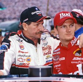dale earnhardt embracing dale earnhardt jr as they stand in their racing gear and baseball caps