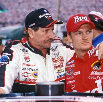 dale earnhardt embracing dale earnhardt jr as they stand in their racing gear and baseball caps