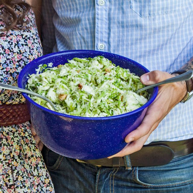 brussels sprout and apple salad in a blue bowl being held by a man's hand