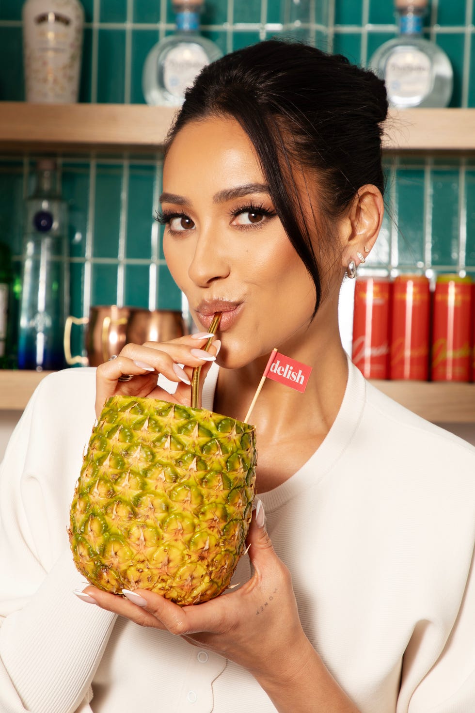 shay mitchell drinking out of a pineapple with delish logo