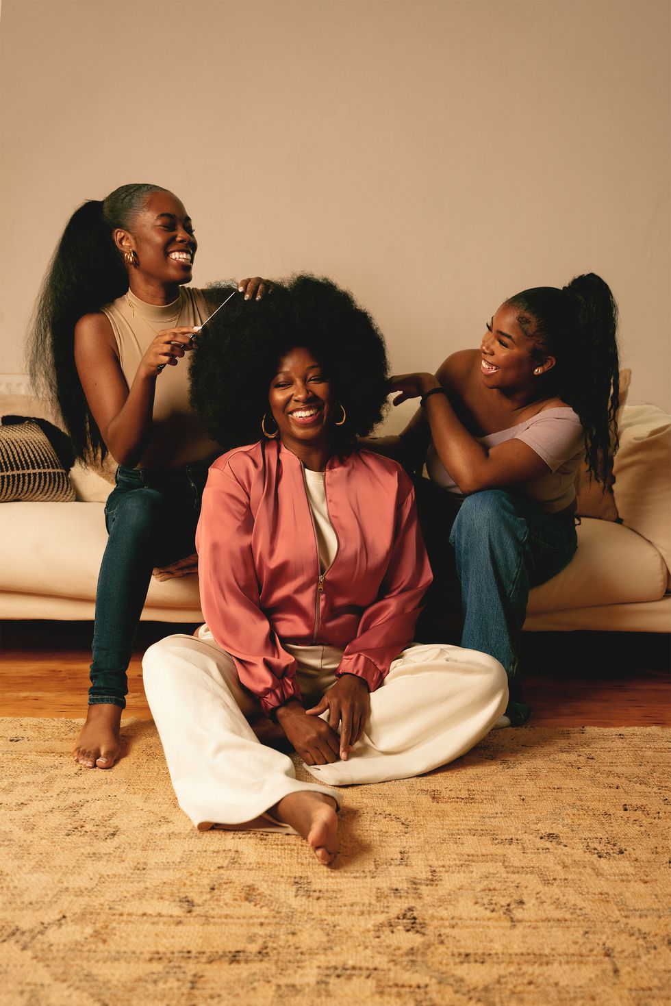 singer jamelia and two of her teen daughters sat on a sofa doing her hair