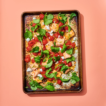 sheet pan with salmon and veggies on a coral background
