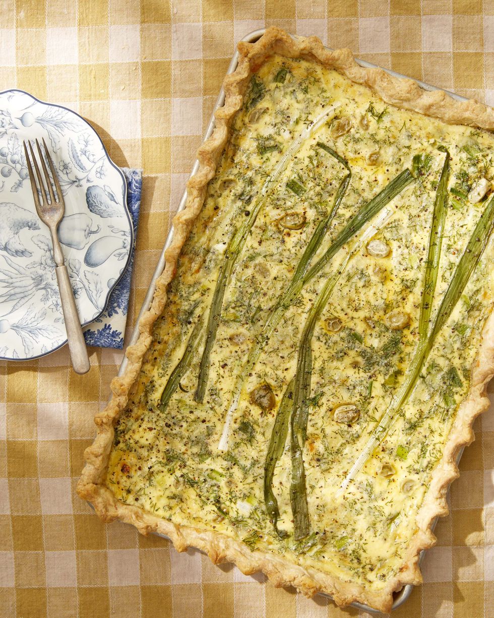 quiche made in a sheet pan set on a yellow and white checked tablecloth with a set of plates to the side