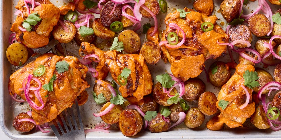 chicken thighs covered in a tikka masala sauce with pickled red onions and jalapenos on a sheet pan
