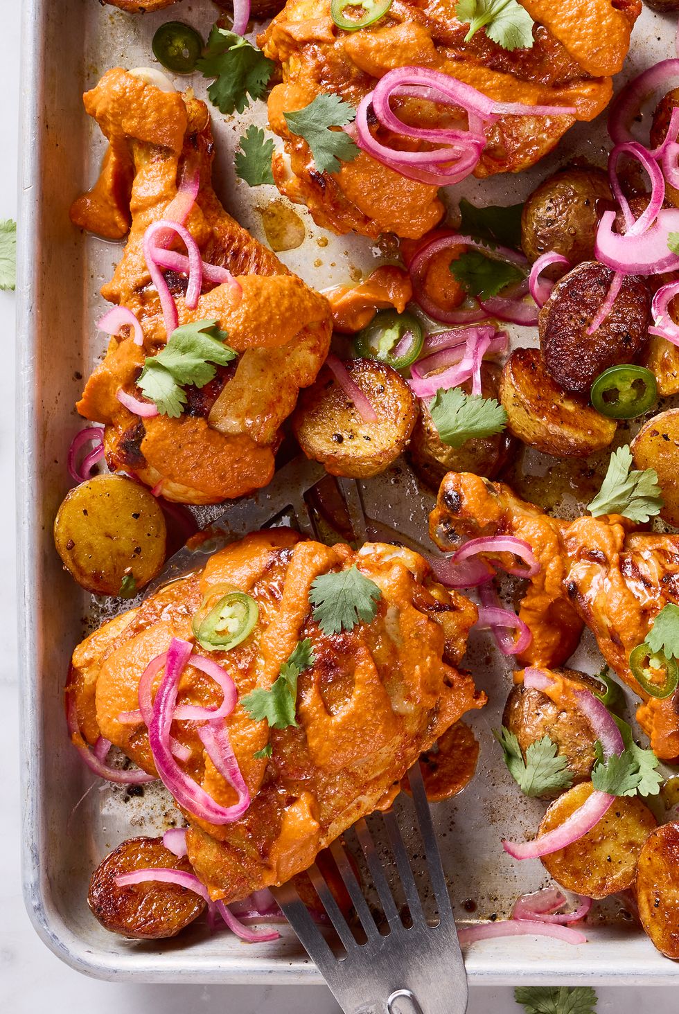 chicken thighs covered in a tikka masala sauce with pickled red onions and jalapenos on a sheet pan