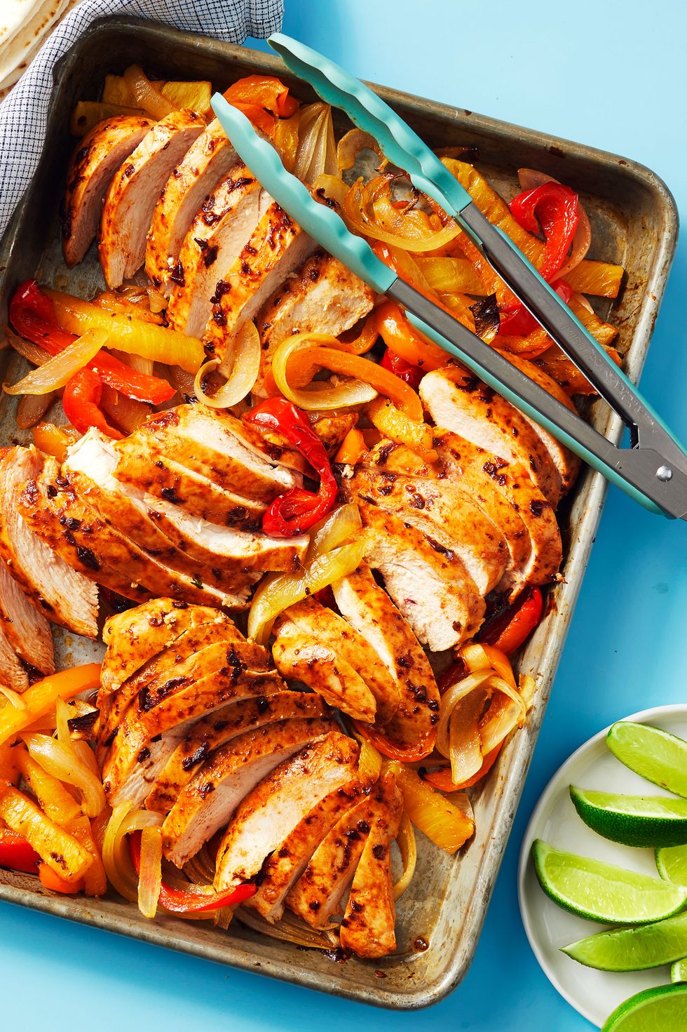 sheet pan chicken fajitas with tongs and a side of limes