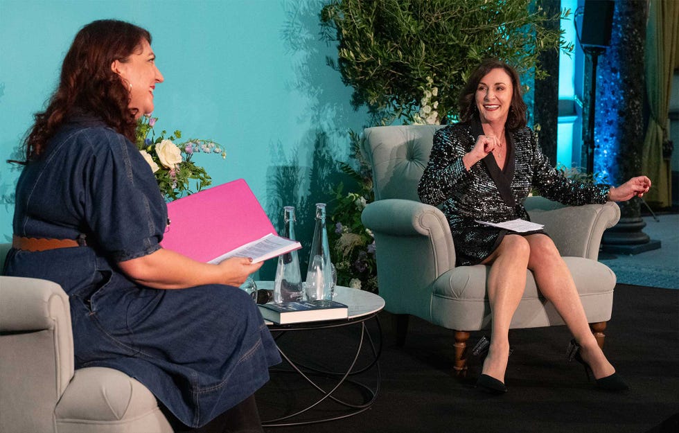 a couple of women sitting on a couch and looking at a book