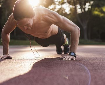 shirtless man exercing push ups on sport field