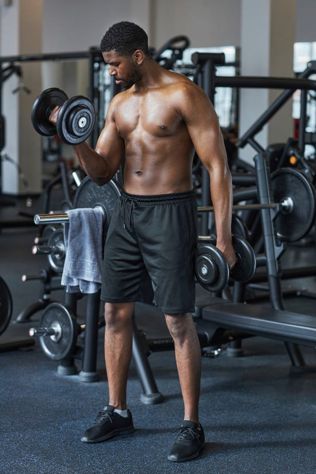 Shirtless man exercising with dumbbells in gym