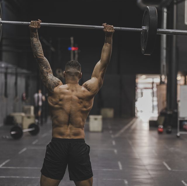 shirtless man in gym lifting dumbbells back